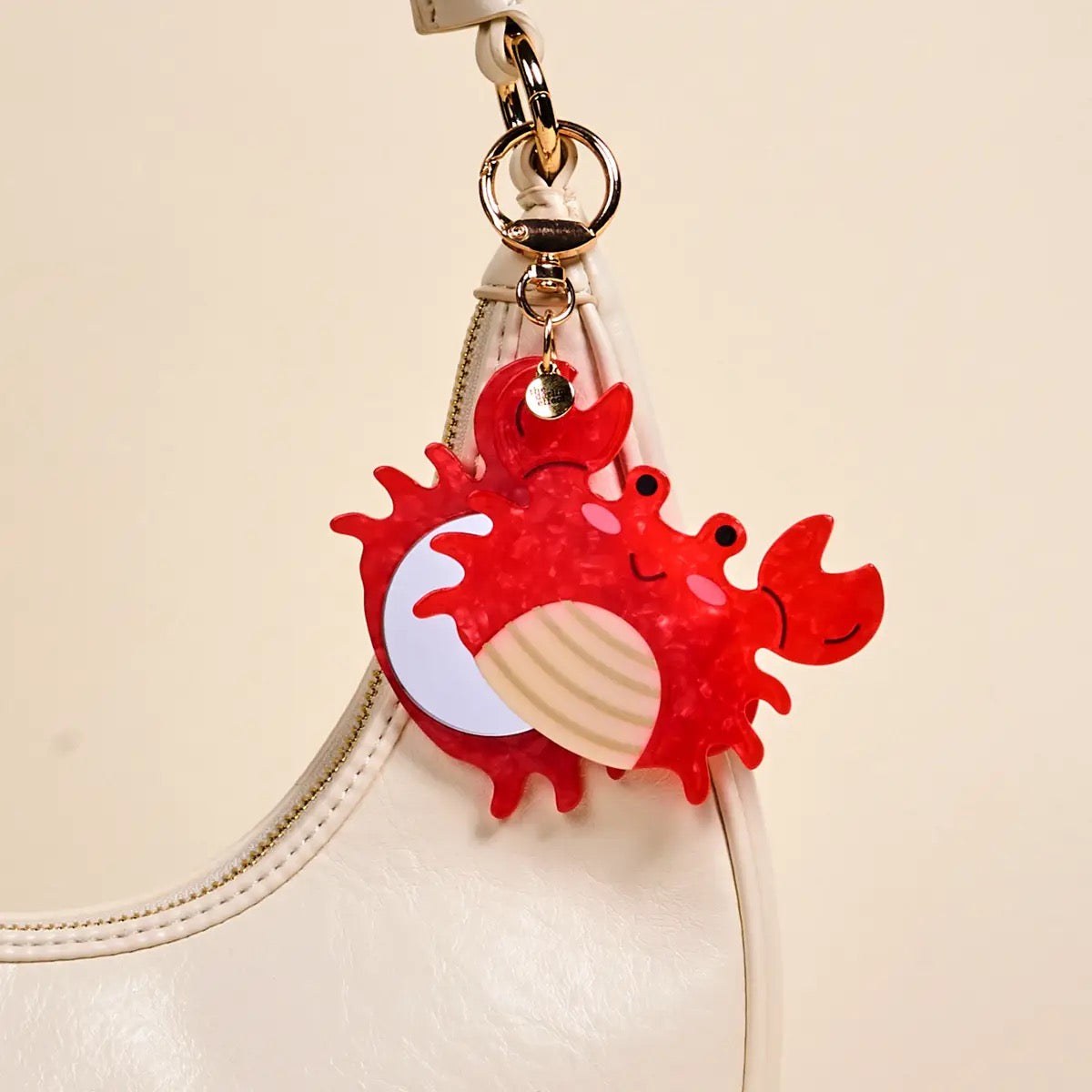Red crab-shaped keychain with a shell on a beige background
