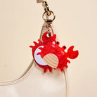 Red crab-shaped keychain with a shell on a beige background