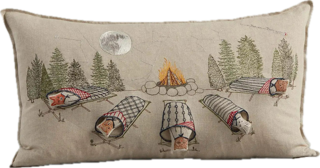 Decorative pillow with camping scene design featuring trees, a campfire, and sleeping bags.