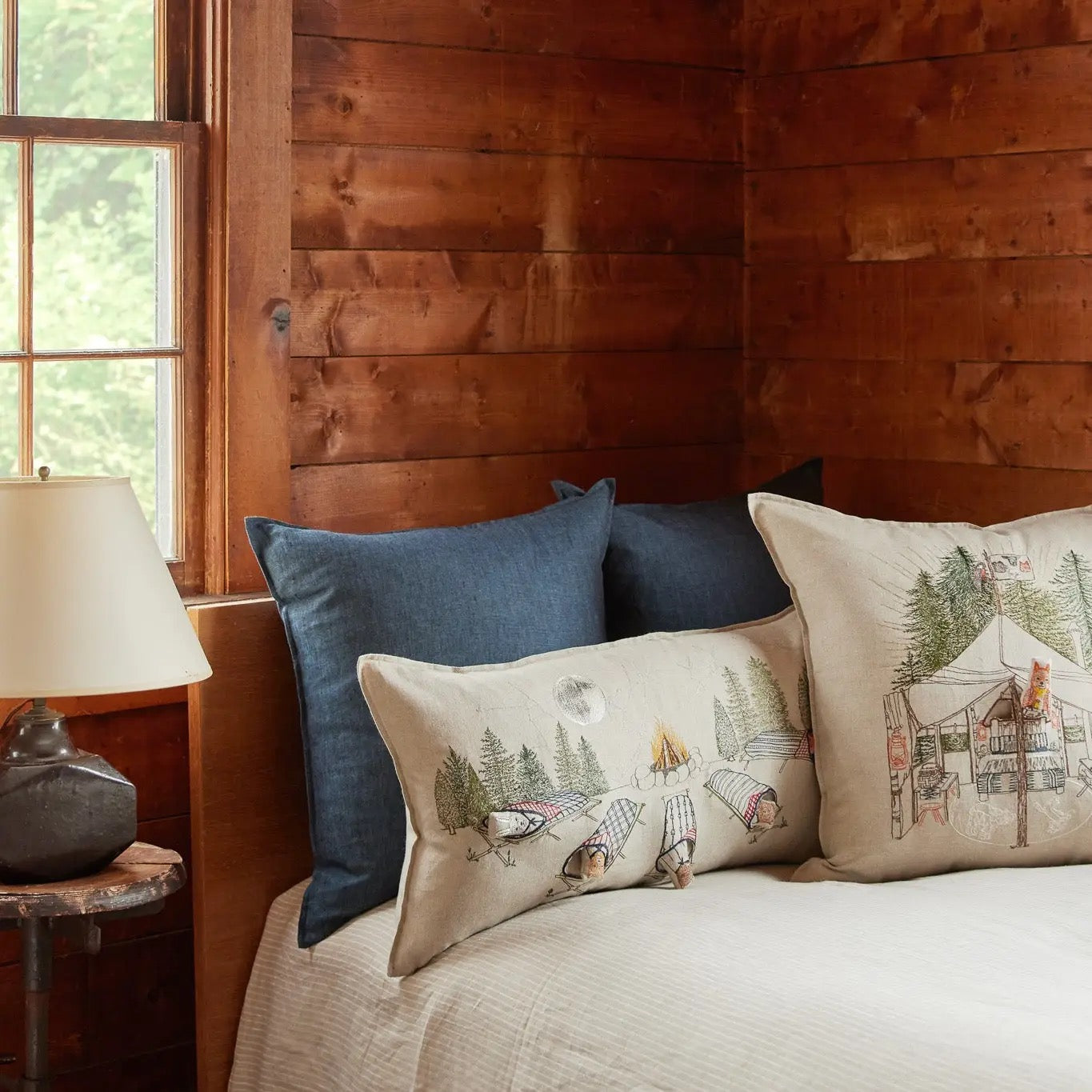 Bed with decorative pillows against a wooden wall with a window.
