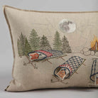 Decorative pillow with embroidered design of foxes in camping chairs by a campfire.
