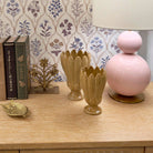 Decorative items including a pink lamp, beige vases, and books on a wooden surface with floral wallpaper.