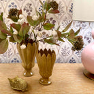 Two decorative vases with floral arrangements on a wooden surface, with a lamp and decorative item in the background.