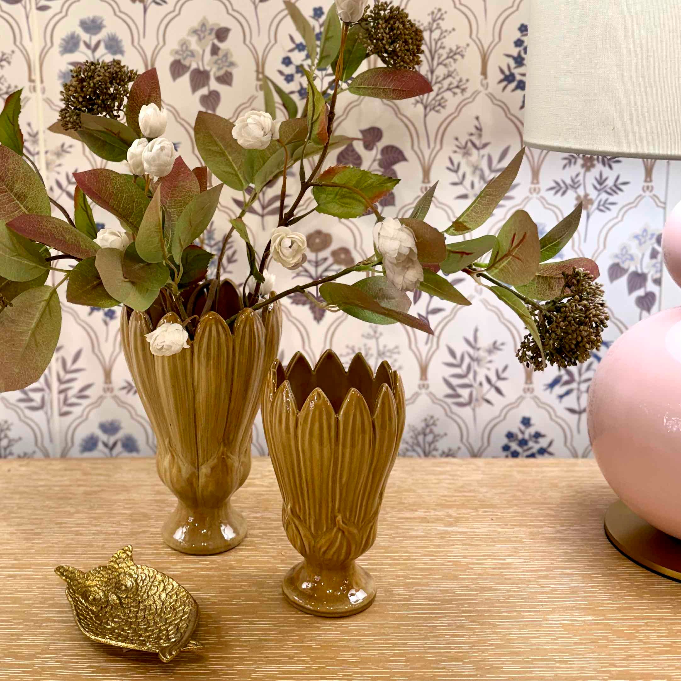 Two decorative vases with floral arrangements on a wooden surface, with a lamp and decorative item in the background.