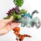 Hand holding three felt dinosaur toys against a white background