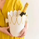 Person holding a decorative wine cooler with a bottle of champagne inside, wearing a yellow dress.