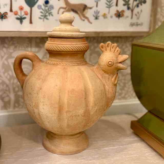 Ceramic vase shaped like a rooster on a surface with a decorative background