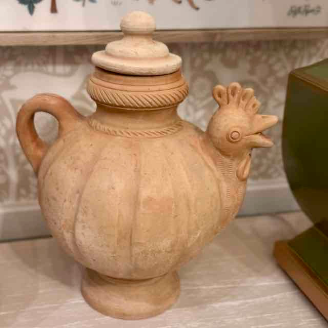Decorative terracotta vase shaped like a chicken on a marble surface.