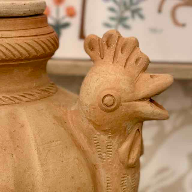 Terracotta jar with a rooster's head on a blurred background