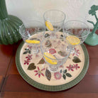 Four cocktail glasses with lemon slices on a decorative tray with floral patterns.
