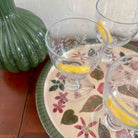 Clear glasses with lemon slices on a floral plate with a green decorative item.