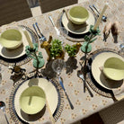Dining table set with green bowls, silverware, and decorative elements on a patterned tablecloth.