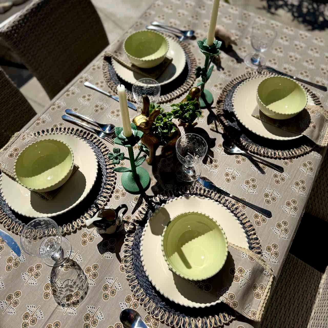 Elegant table setting with green bowls and silverware on a patterned tablecloth.