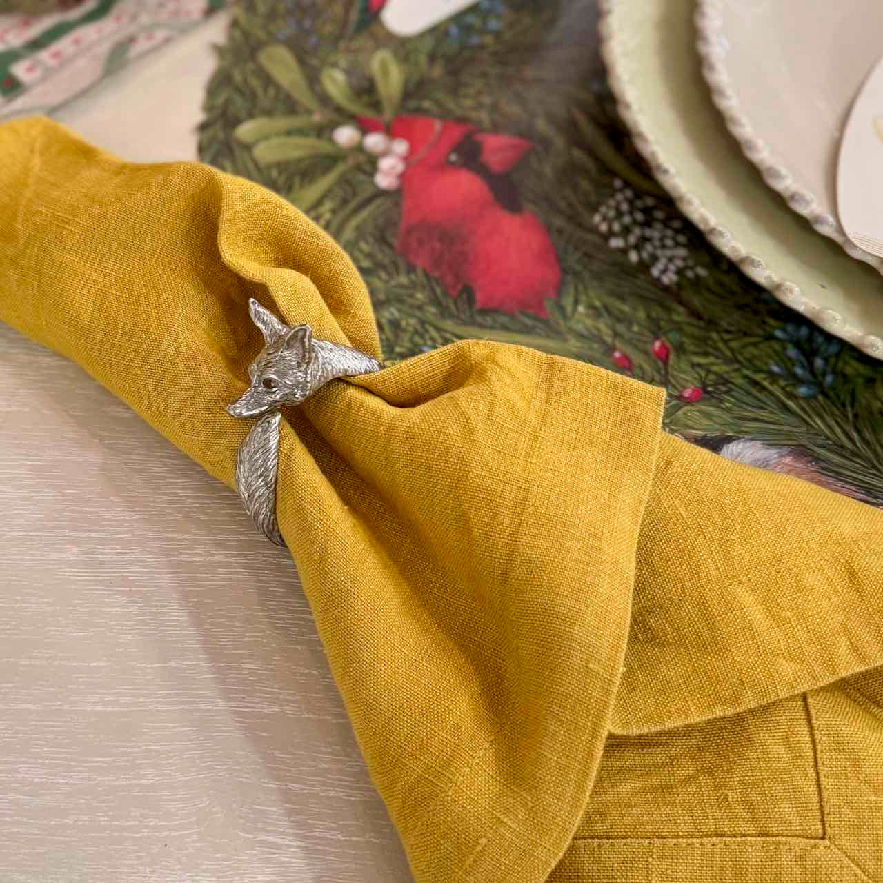 Yellow napkin with a silver fox-shaped napkin ring on a decorative table setting.