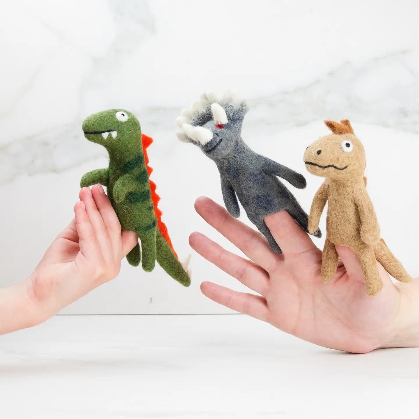 Three small plush toys held in hands against a light background