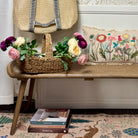 Decorative scene with a woven basket, flowers, books, and a floral-patterned pillow on a bench.