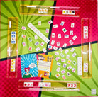 A colorful board game set with multiple translucent acrylic slots holding playing cards, scattered cards across a bright geometric background, a blue illustrated instruction card, and a small white box. The layout is photographed from above on a bold pink, green, and yellow graphic surface.
