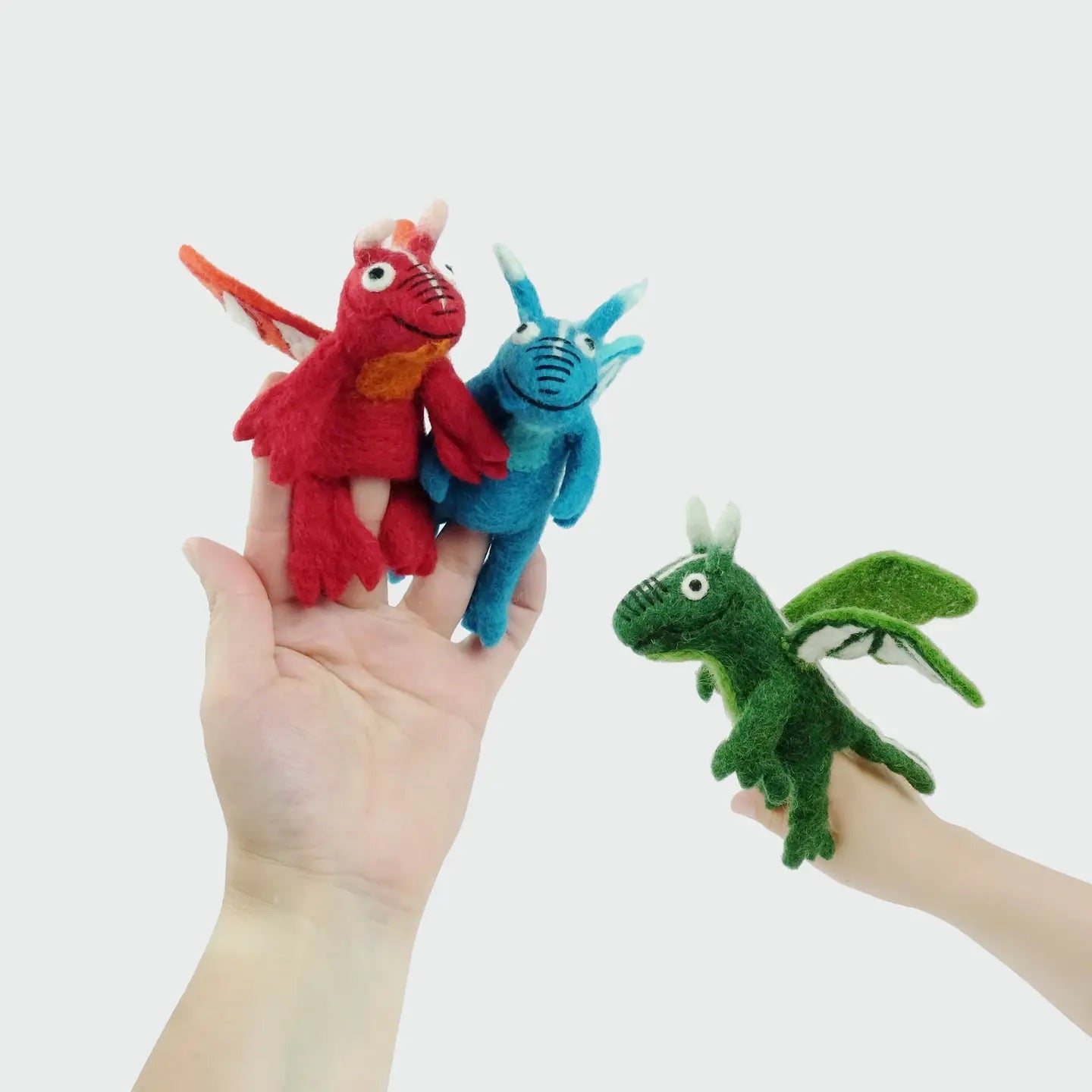 Three colorful dragon finger puppets held by a hand against a white background