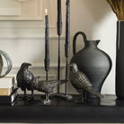 Decorative birds, candlesticks, and a vase on a shelf with a neutral background