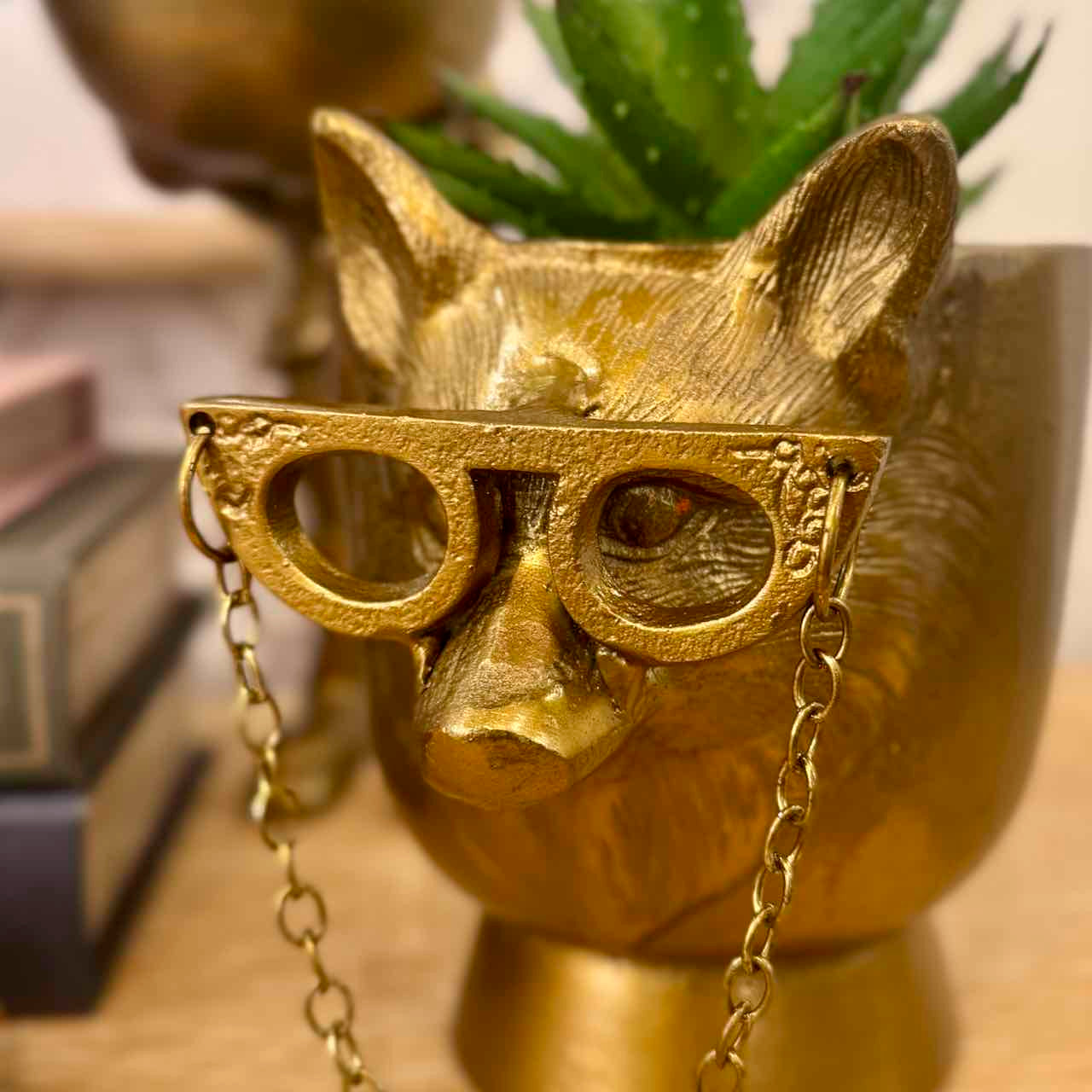 Gold cat-shaped object with glasses and a chain on a wooden surface