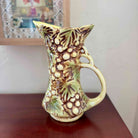 Decorative ceramic pitcher with leaf patterns on a wooden surface.