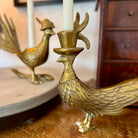 Gold peacock-shaped candle holder with a candle on a wooden surface.