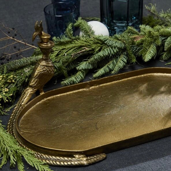 Gold decorative tray with a handle on a dark surface with greenery