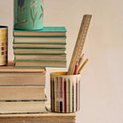Stack of books with a container holding pencils and a ruler on a beige background