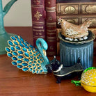 Decorative peacock figurine with other small objects on a wooden surface.