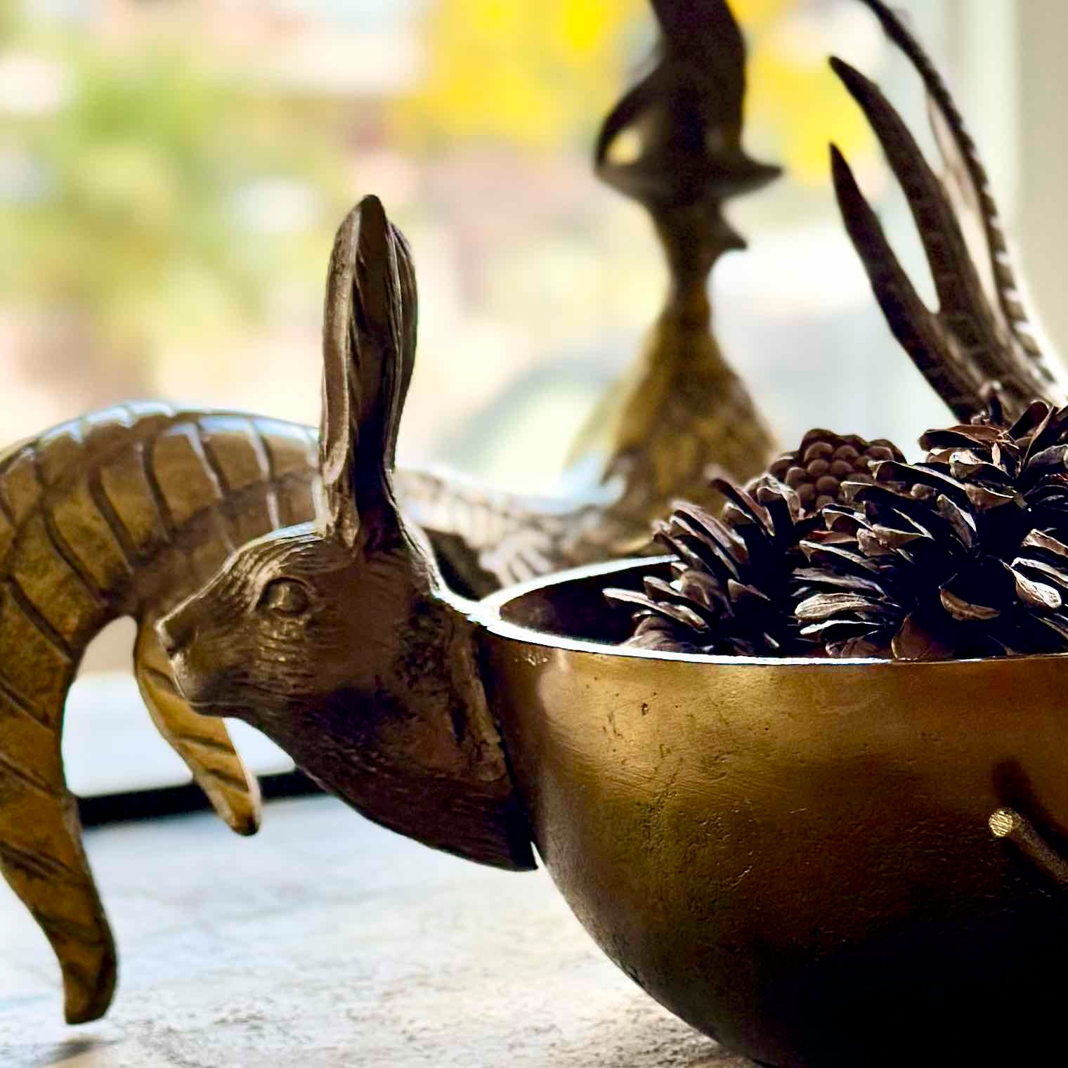 Bronze rabbit figurine with a bowl of pinecones on a blurred background