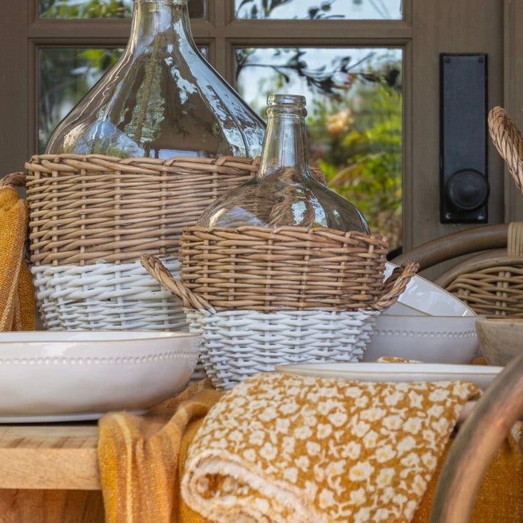 Decorative setting with wicker baskets, glass bottles, and a floral towel on a table.