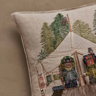 Close-up of a beige linen throw pillow featuring embroidered camping scene with a canvas tent, pine trees, and two bear characters in winter clothing.