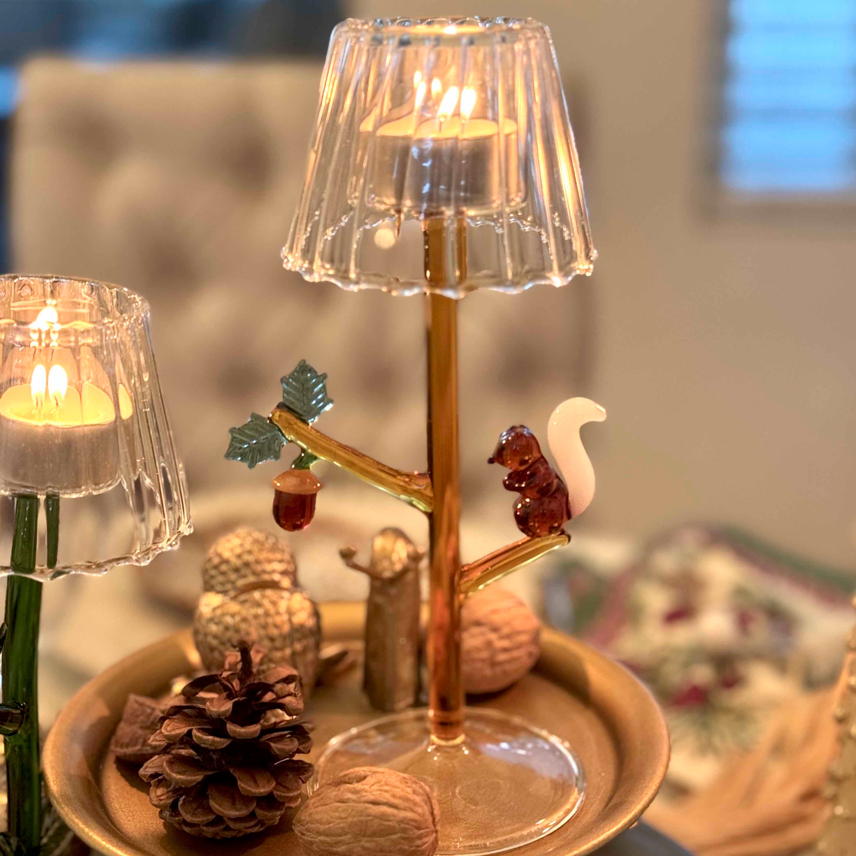 Decorative lamp with a squirrel figure on a table with pinecones and candles.