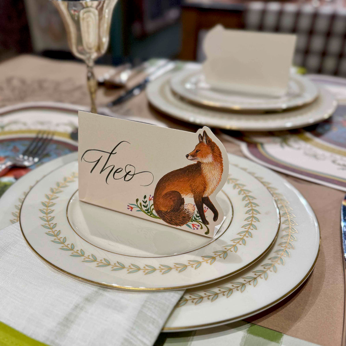 Table setting with decorative plates and a card featuring a fox illustration.