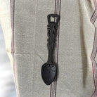 Decorative black spoon bottle opener on a textured fabric background