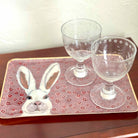 Two glasses on a decorative tray with a rabbit design on a wooden surface.