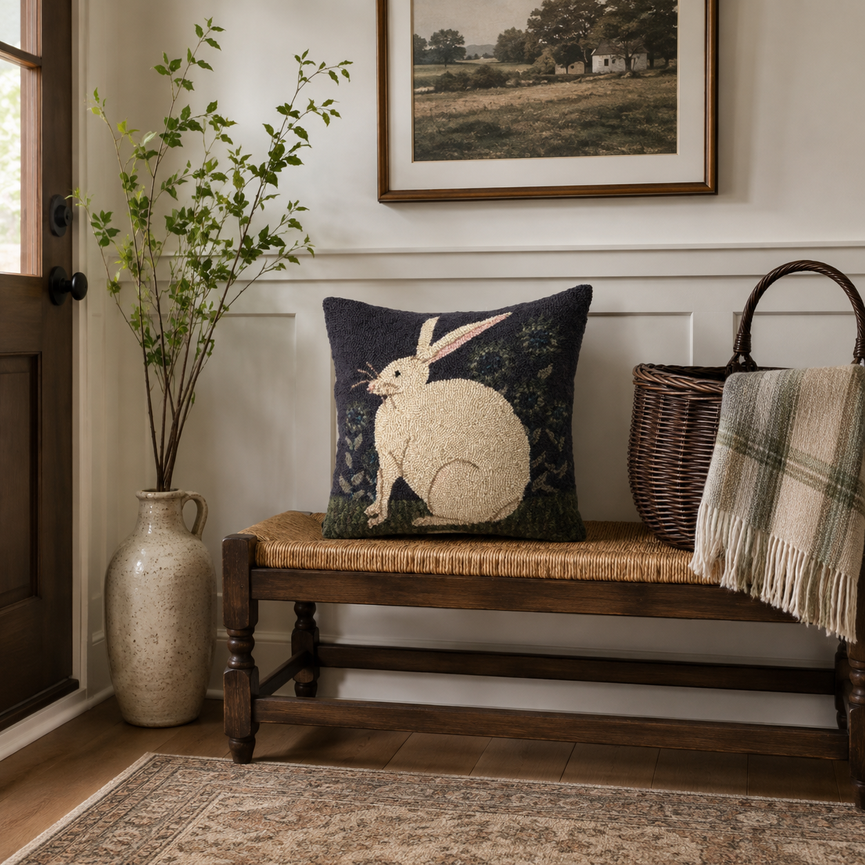 A decorative throw pillow featuring a white embroidered rabbit on a dark navy blue background, styled on a wooden bench in a cozy, rustic room setting.