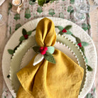 Yellow napkin with a decorative flower on a Christmas-themed table setting.