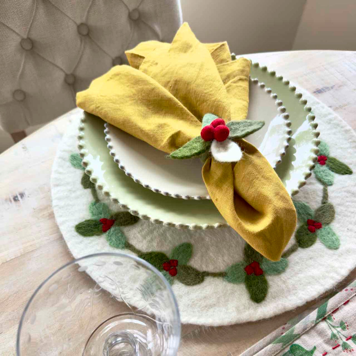 Decorative table setting with a yellow napkin and holly berry decoration on a white plate.