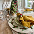 Dining table set with Christmas decorations, including a small tree and holly-patterned plates.