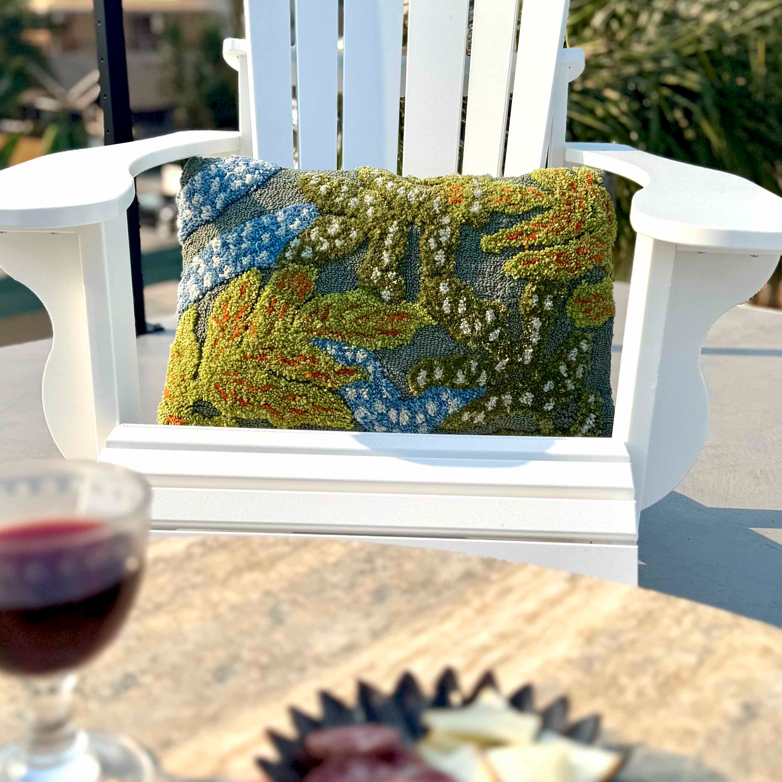 Decorative pillow on a white chair with a glass of red wine and plate of snacks on a table.