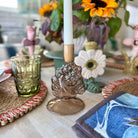 Decorative candle holder with a white candle on a table with a glass, flowers, and other decorative items.
