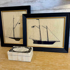 Two framed illustrations of ships on a wooden surface with a decorative box.
