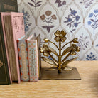 Gold floral bookend on a wooden surface with books and decorative wallpaper in the background