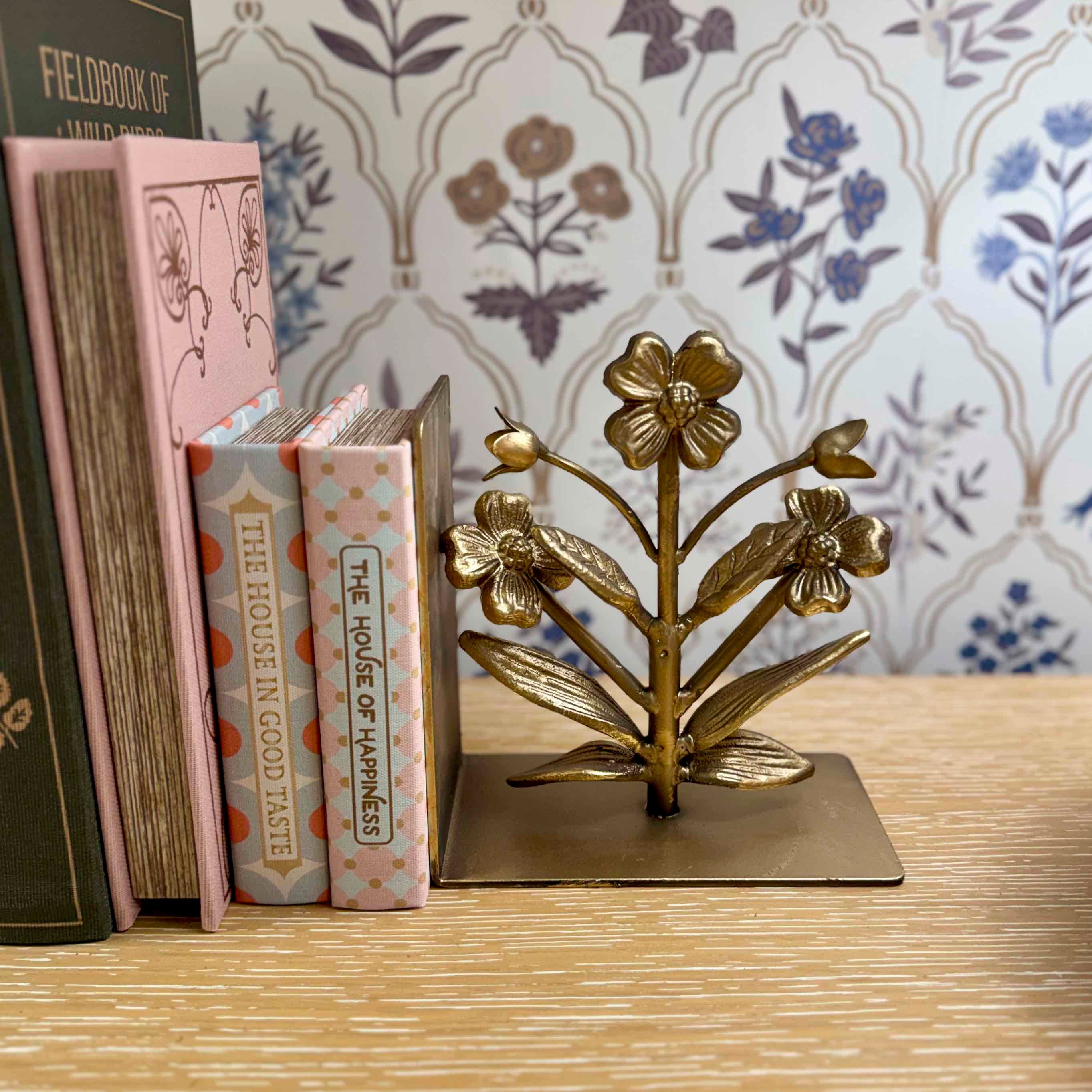 Gold floral bookend on a wooden surface with books and decorative wallpaper in the background