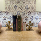 Decorative books with gold leaf stands on a wooden surface against a floral wallpaper background