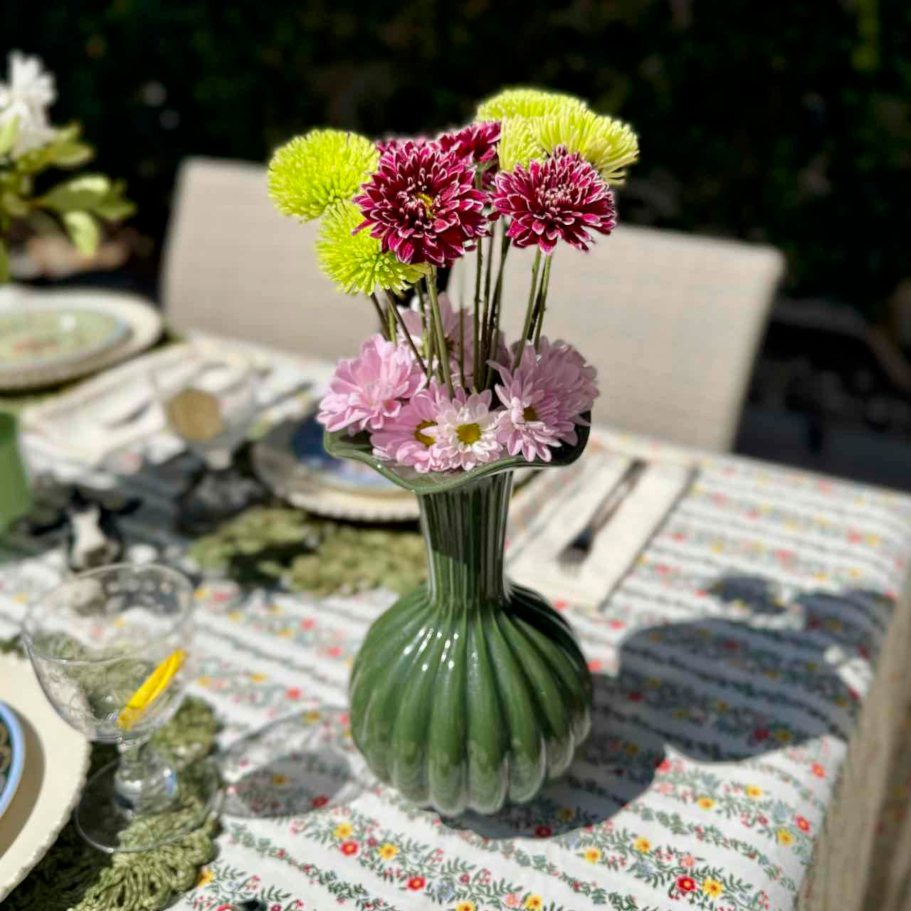 Green vase with flowers on a table set for dinner outdoors