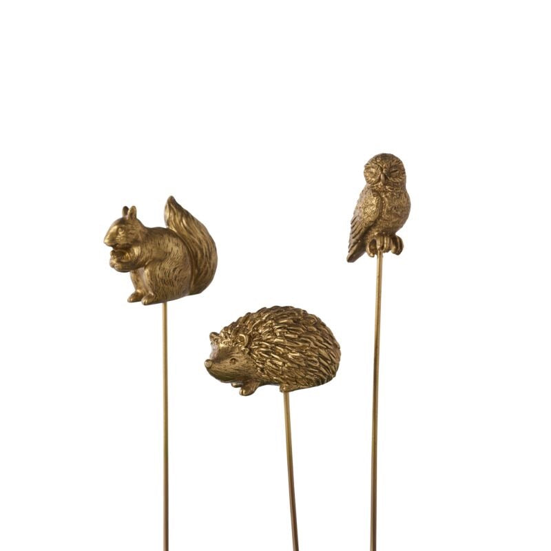 Three gold animal figurines on sticks (squirrel, owl, hedgehog) against a white background