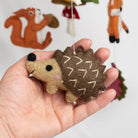 Hand holding a small hedgehog plush toy with a blurred background of other animal toys.