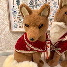 Stuffed fox toy wearing a red outfit with white trim against a decorative wall.